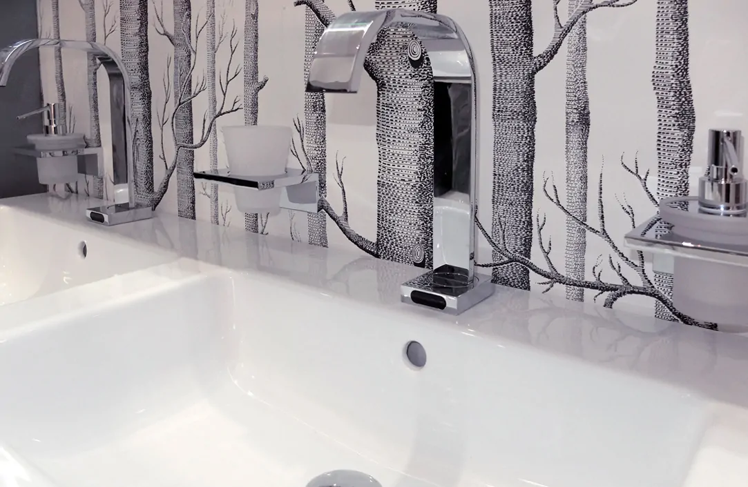 Modern bathroom sink with chrome taps and artistic tree-patterned wallpaper.