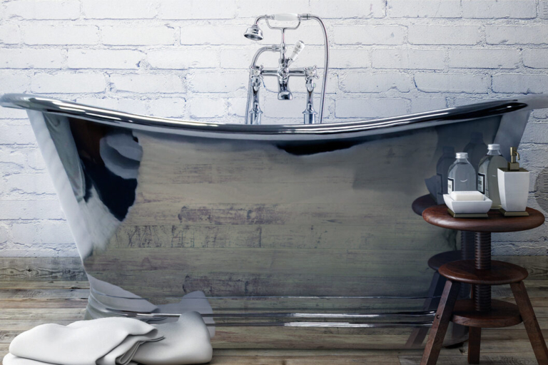 A sleek, curved bathtub is positioned against a white brick wall with a wooden stool nearby.
