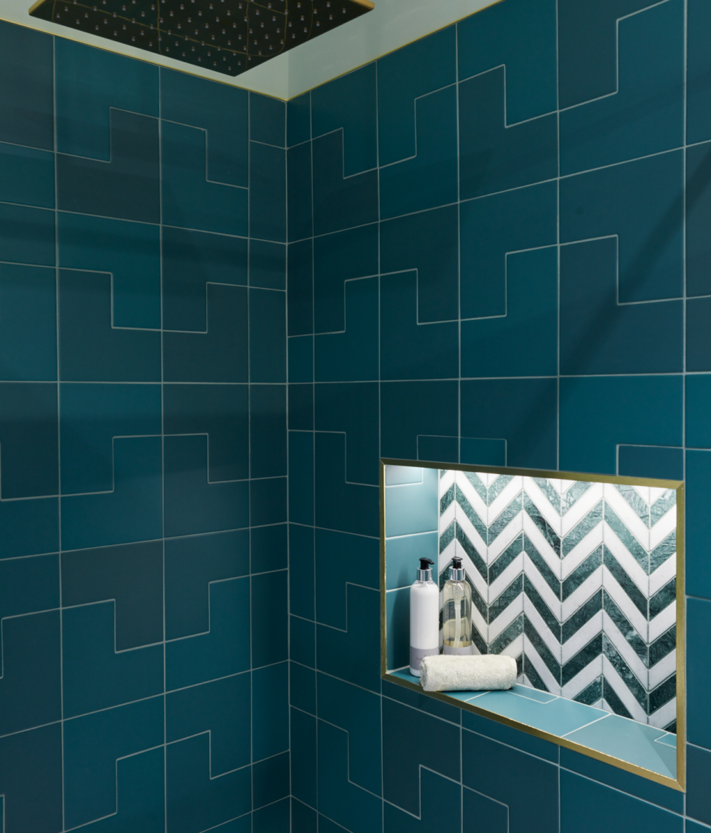 A modern shower area featuring teal tiles, gold accents, and a recessed shelf.