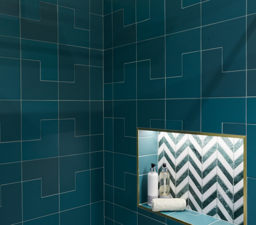 A modern shower area featuring teal tiles, gold accents, and a recessed shelf.