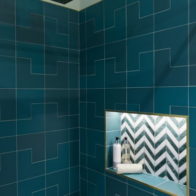 A modern shower area featuring teal tiles, gold accents, and a recessed shelf.