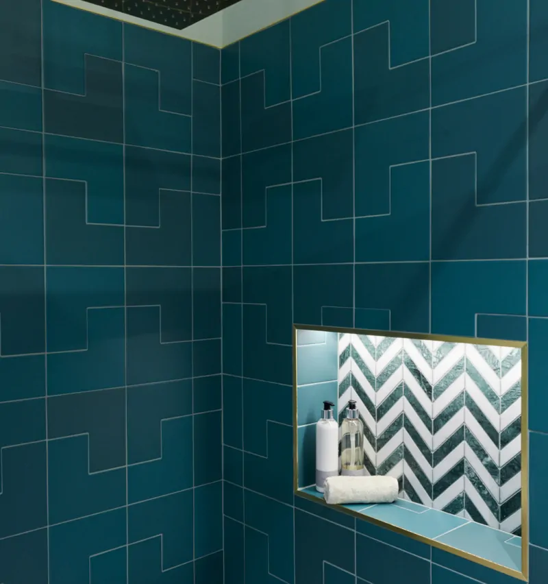 A modern shower area featuring teal tiles, gold accents, and a recessed shelf.