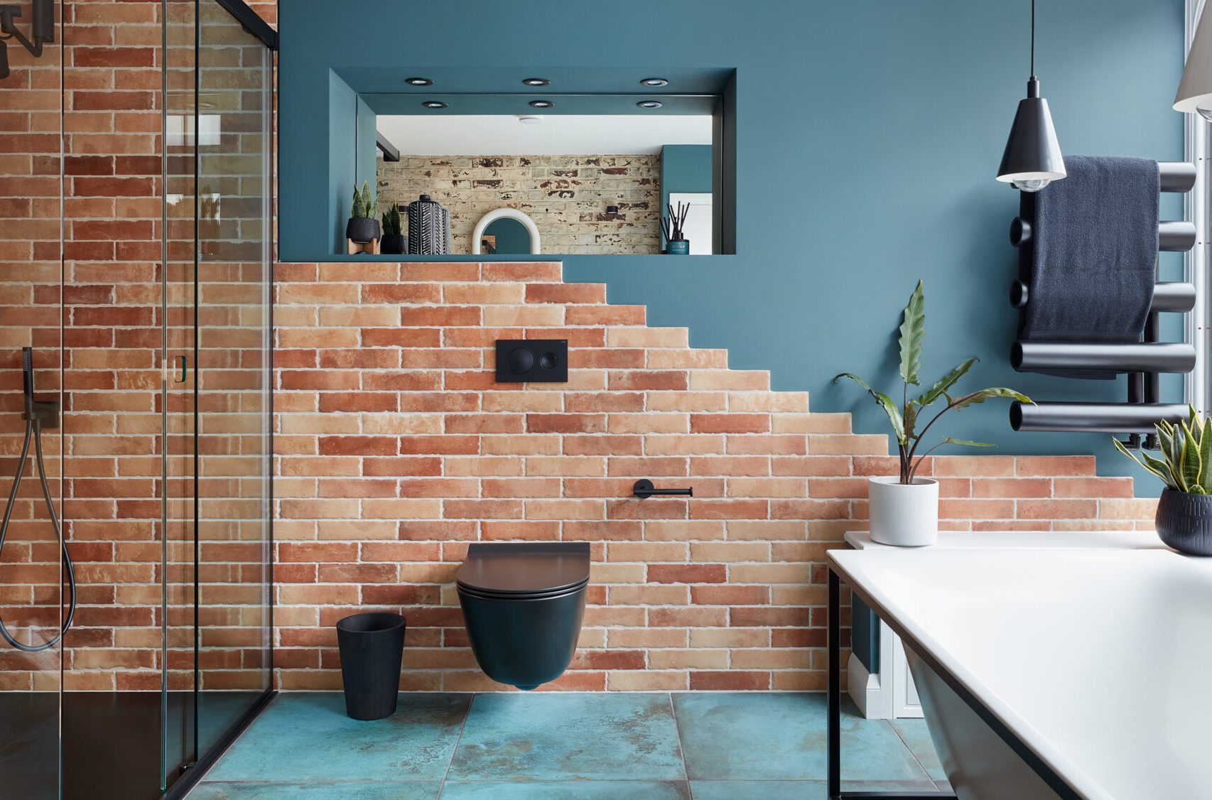 Modern bathroom with brick walls, glass shower, plant accents, and stylish fixtures.