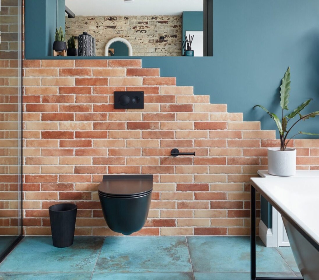 Modern bathroom with brick walls, glass shower, plant accents, and stylish fixtures.