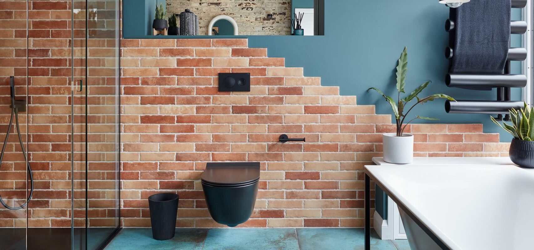 Modern bathroom with brick walls, glass shower, plant accents, and stylish fixtures.