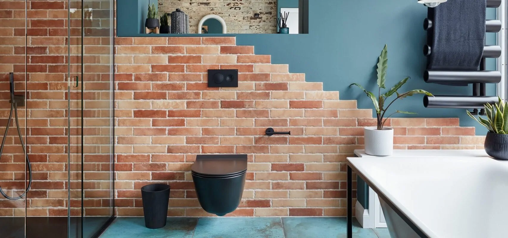 Modern bathroom with brick walls, glass shower, plant accents, and stylish fixtures.