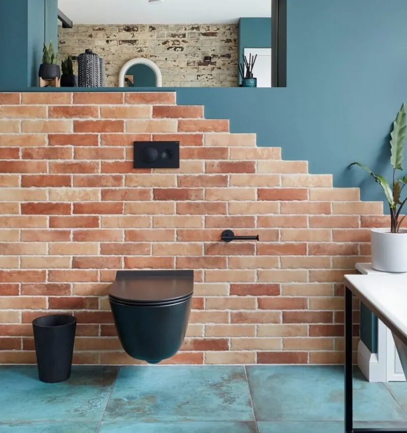 Modern bathroom with brick walls, glass shower, plant accents, and stylish fixtures.