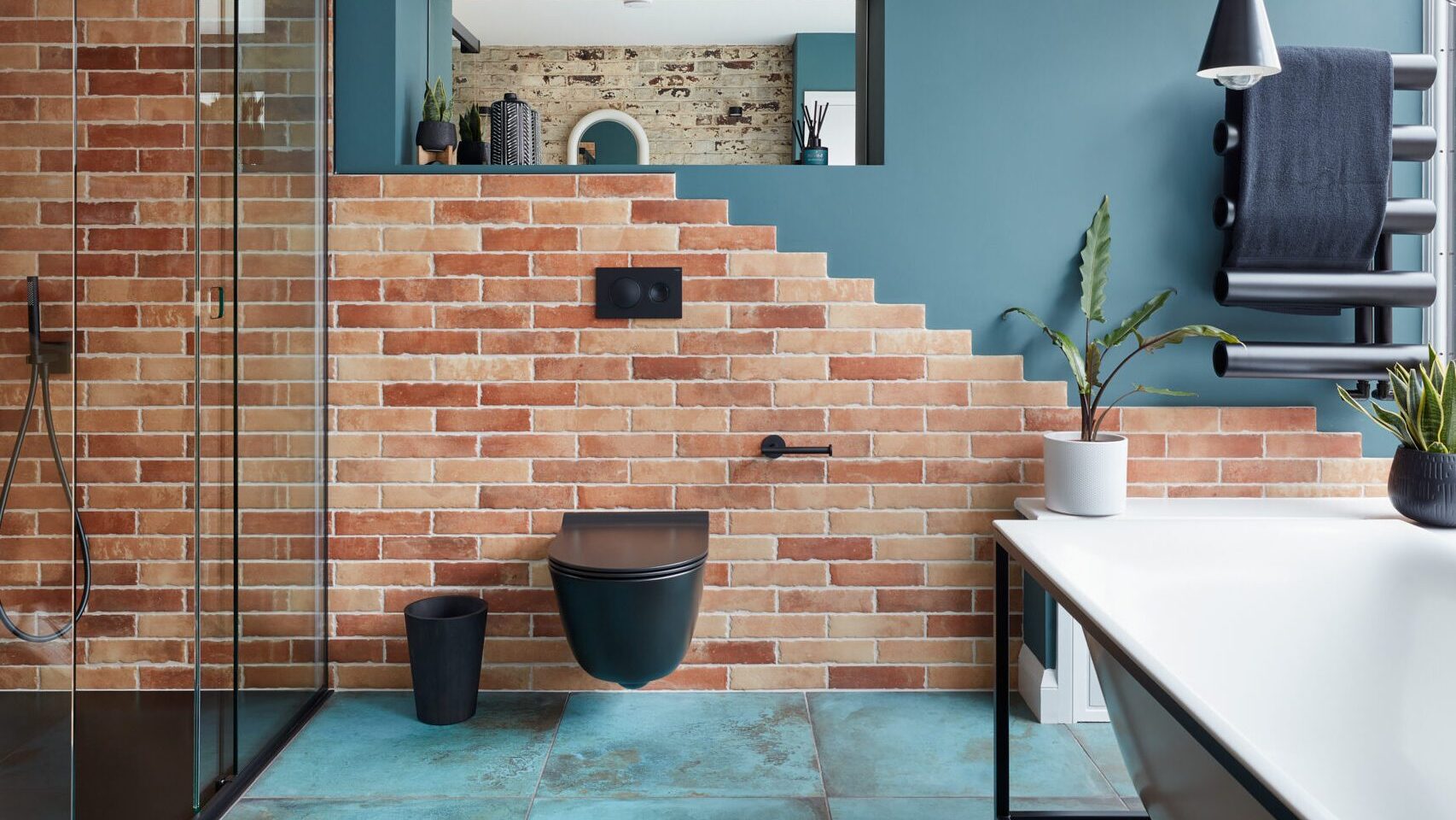 Modern bathroom with brick walls, glass shower, plant accents, and stylish fixtures.
