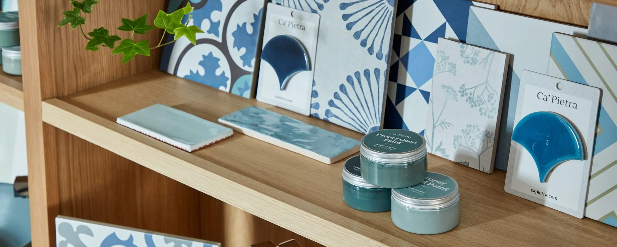 A wooden shelving unit displaying various patterned tiles and paint samples in blue tones.