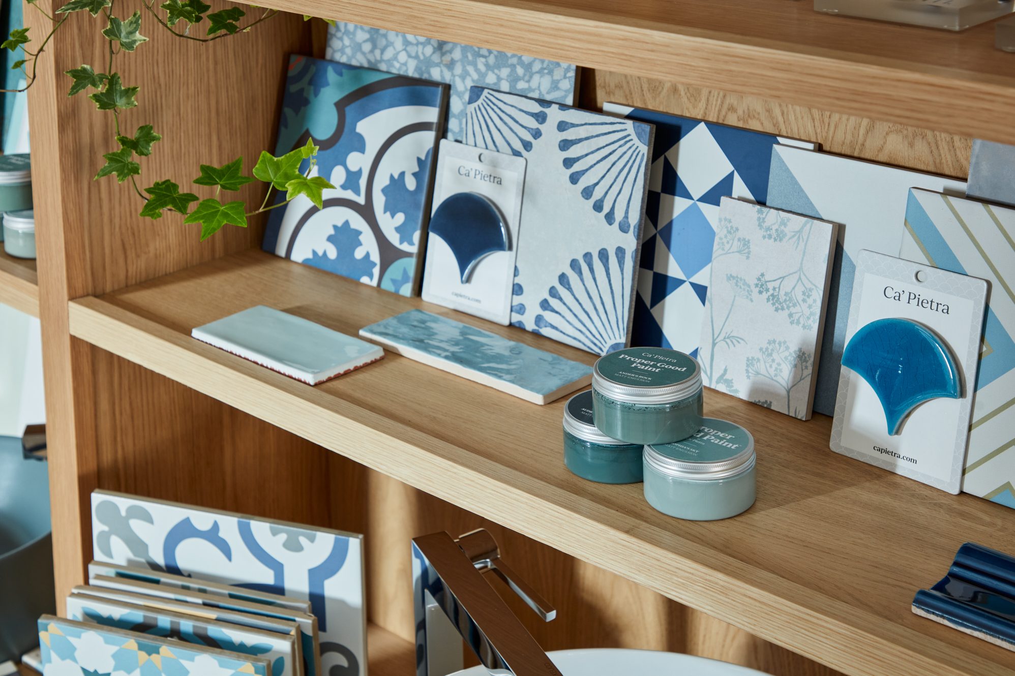 A wooden shelving unit displaying various patterned tiles and paint samples in blue tones.