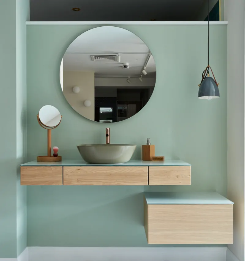 Modern bathroom featuring a circular mirror, wooden vanity, and terrazzo floor.