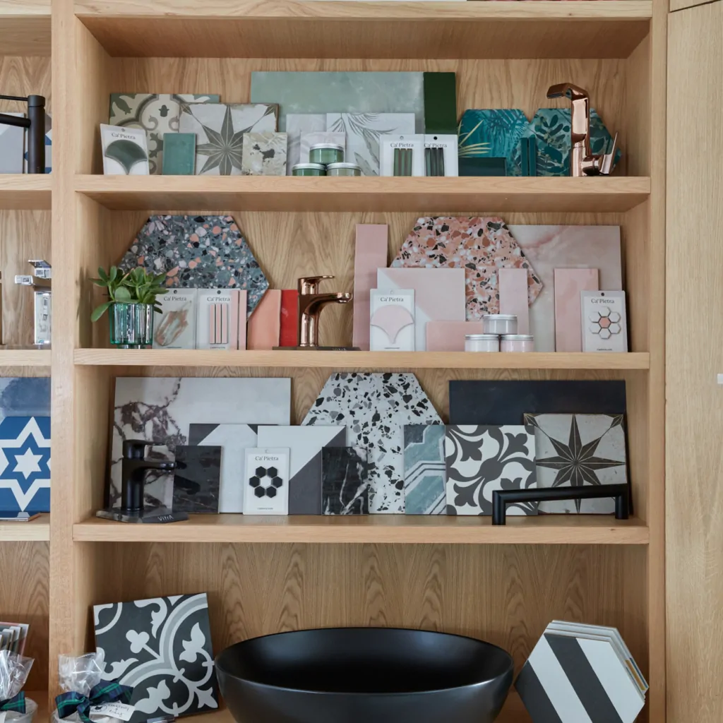 Shelves display various tiles, materials, a black bowl, and decorative items in a studio.