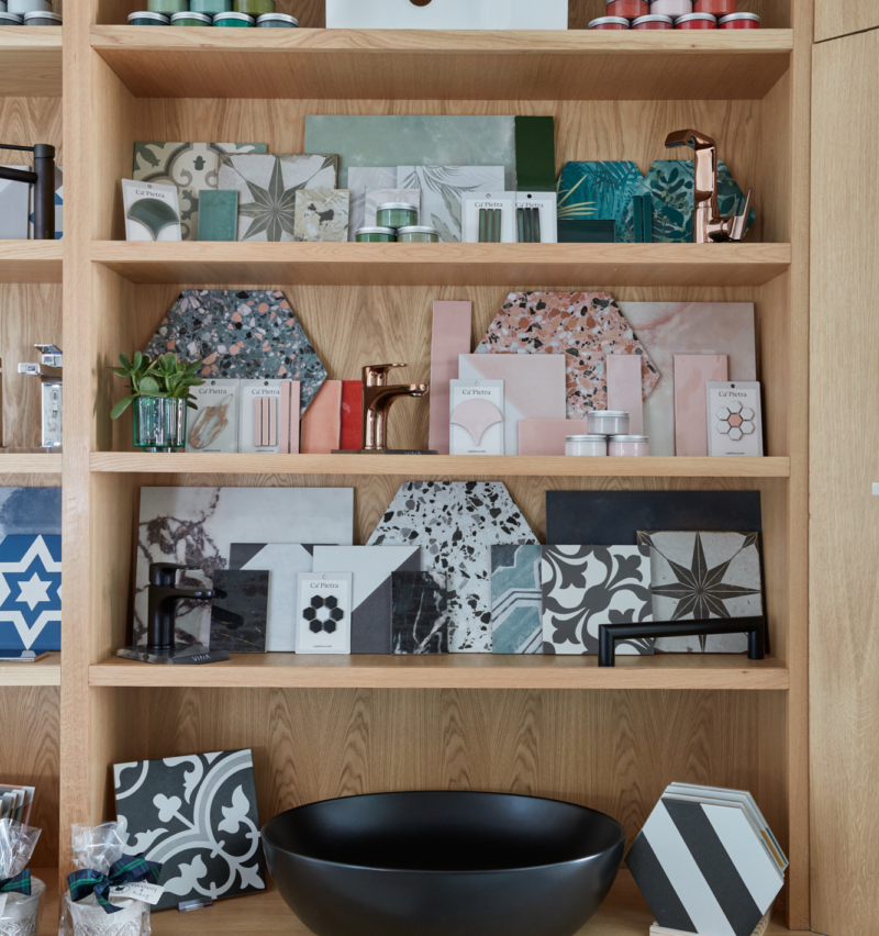 Shelves display various tiles, materials, a black bowl, and decorative items in a studio.