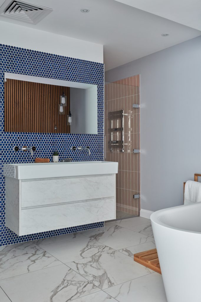Modern bathroom with blue tile backsplash, floating vanity, and freestanding bathtub.