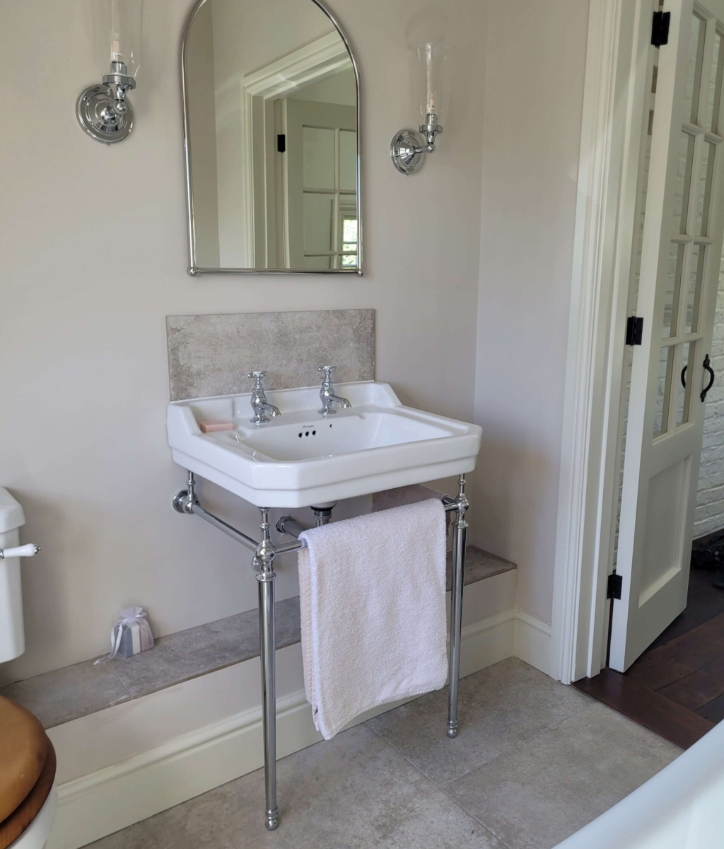 Classic white sink with chrome taps and exposed pipes, paired with a curved mirror and wall-mounted lighting fixtures