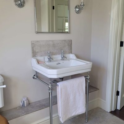 Classic white sink with chrome taps and exposed pipes, paired with a curved mirror and wall-mounted lighting fixtures