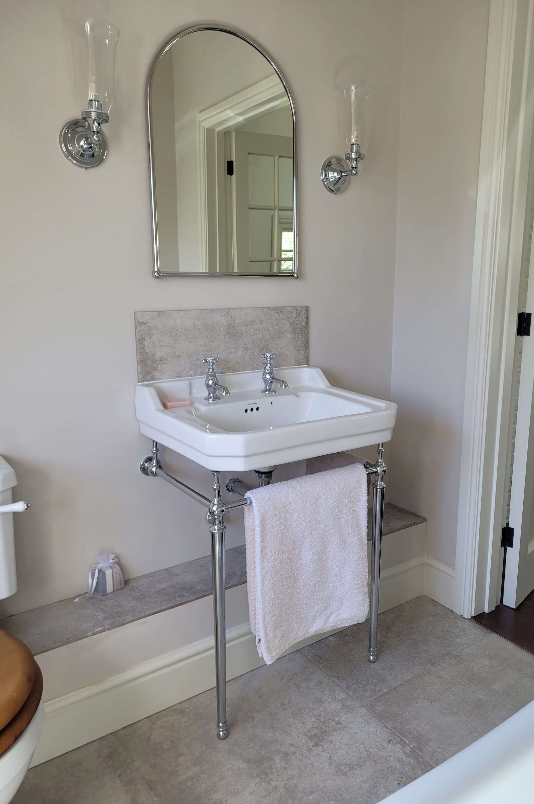 Classic white sink with chrome taps and exposed pipes, paired with a curved mirror and wall-mounted lighting fixtures