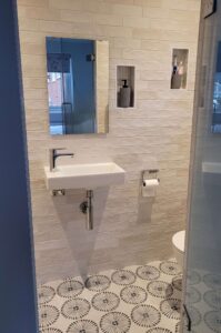 Compact bathroom with white subway tiles, floating sink, and modern patterned floor tiles