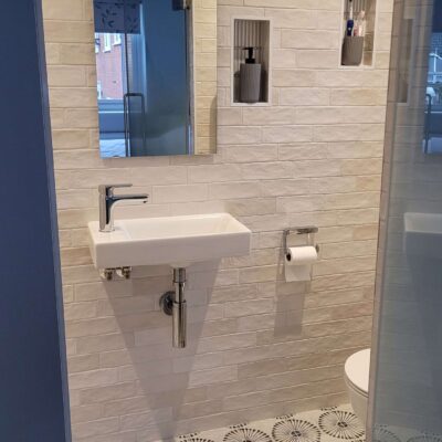 Compact bathroom with white subway tiles, floating sink, and modern patterned floor tiles