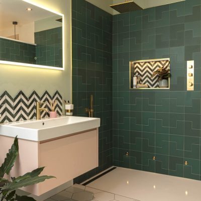 Contemporary bathroom with dark green geometric tiles, gold fixtures, illuminated mirror, and chevron accent tiles in the shower.