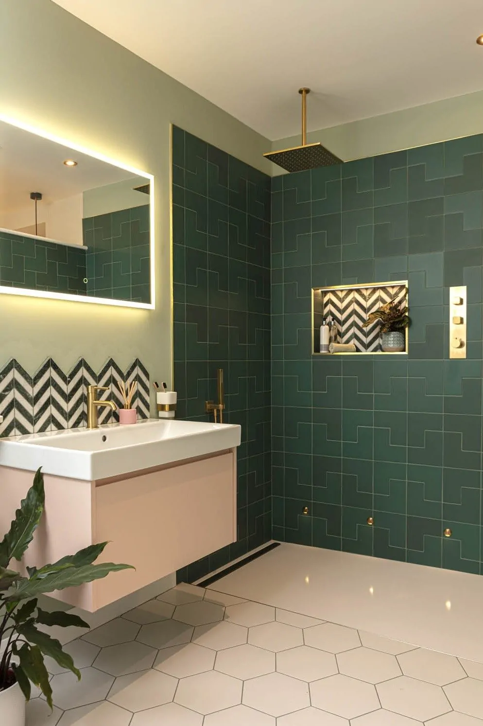 Contemporary bathroom with dark green geometric tiles, gold fixtures, illuminated mirror, and chevron accent tiles in the shower.