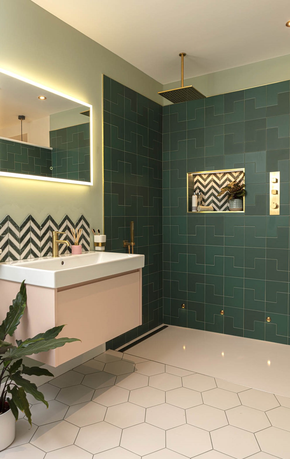 Contemporary bathroom with dark green geometric tiles, gold fixtures, illuminated mirror, and chevron accent tiles in the shower.