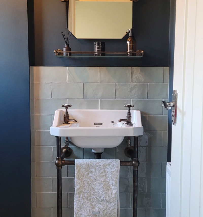 Dark-themed bathroom with a vintage-style wall-mounted sink, bronze fittings, and deep blue walls