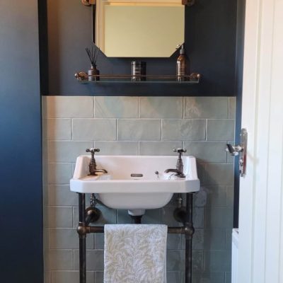 Dark-themed bathroom with a vintage-style wall-mounted sink, bronze fittings, and deep blue walls