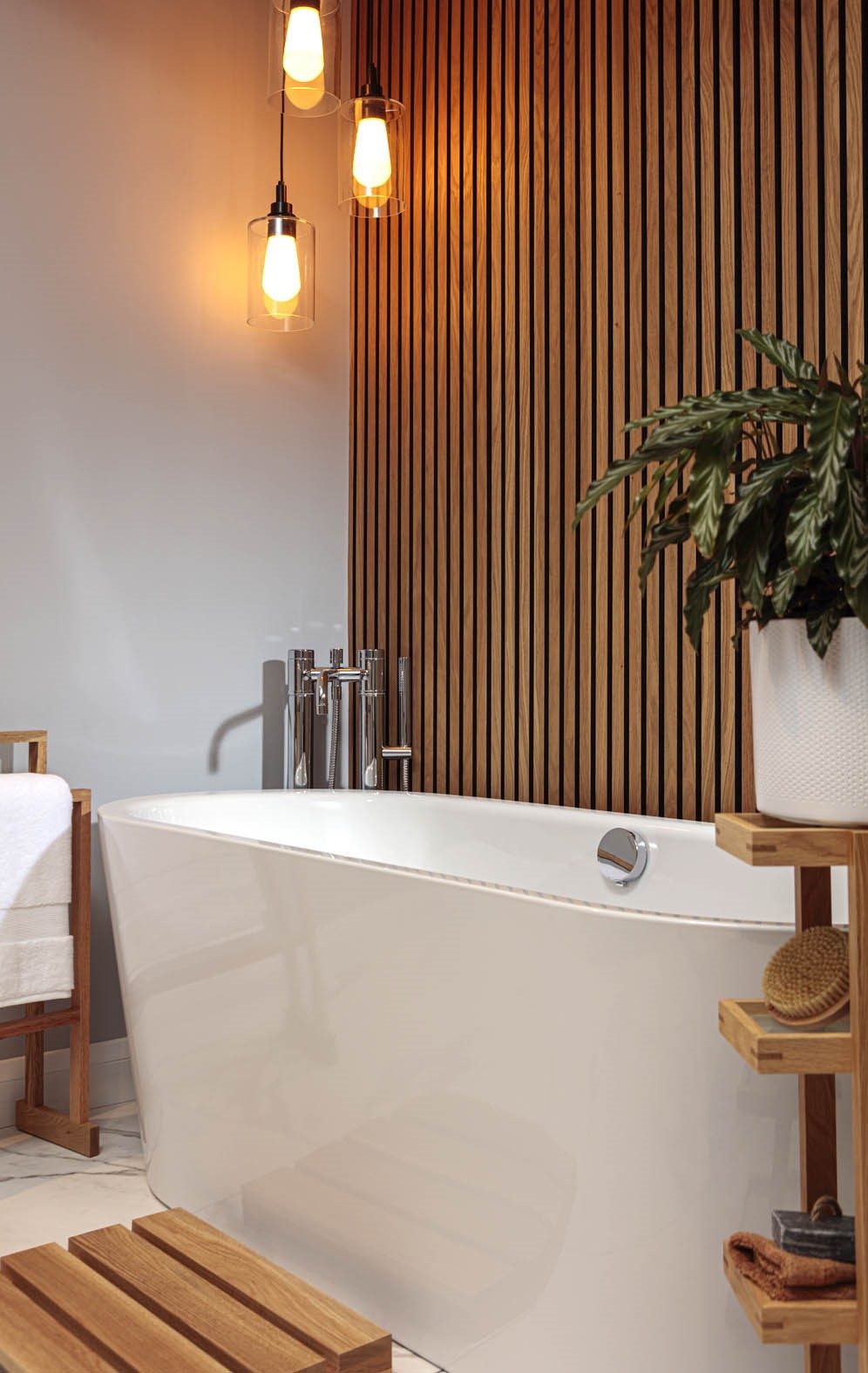 Freestanding bathtub with chrome fixtures, a wooden slat feature wall, warm hanging pendant lights, and natural wood accents