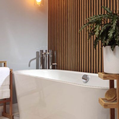 Freestanding bathtub with chrome fixtures, a wooden slat feature wall, warm hanging pendant lights, and natural wood accents