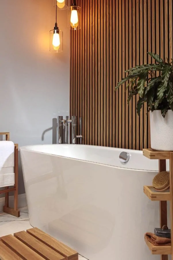 Freestanding bathtub with chrome fixtures, a wooden slat feature wall, warm hanging pendant lights, and natural wood accents