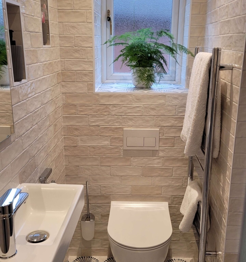 Narrow modern bathroom featuring a small floating sink, white subway tiles, and a large window with a potted plant