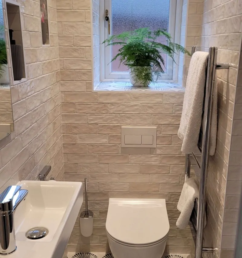 Narrow modern bathroom featuring a small floating sink, white subway tiles, and a large window with a potted plant
