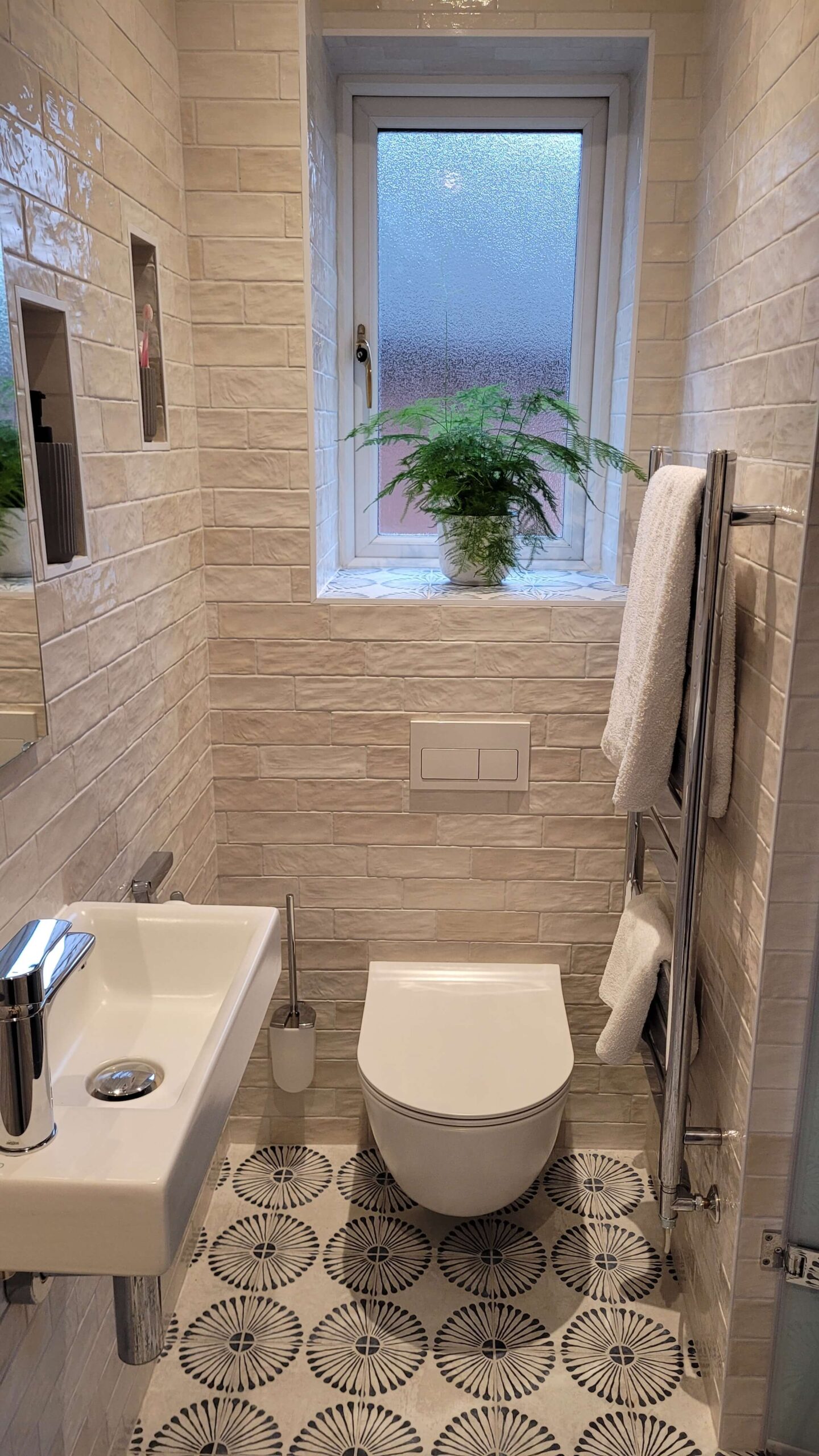 Narrow modern bathroom featuring a small floating sink, white subway tiles, and a large window with a potted plant