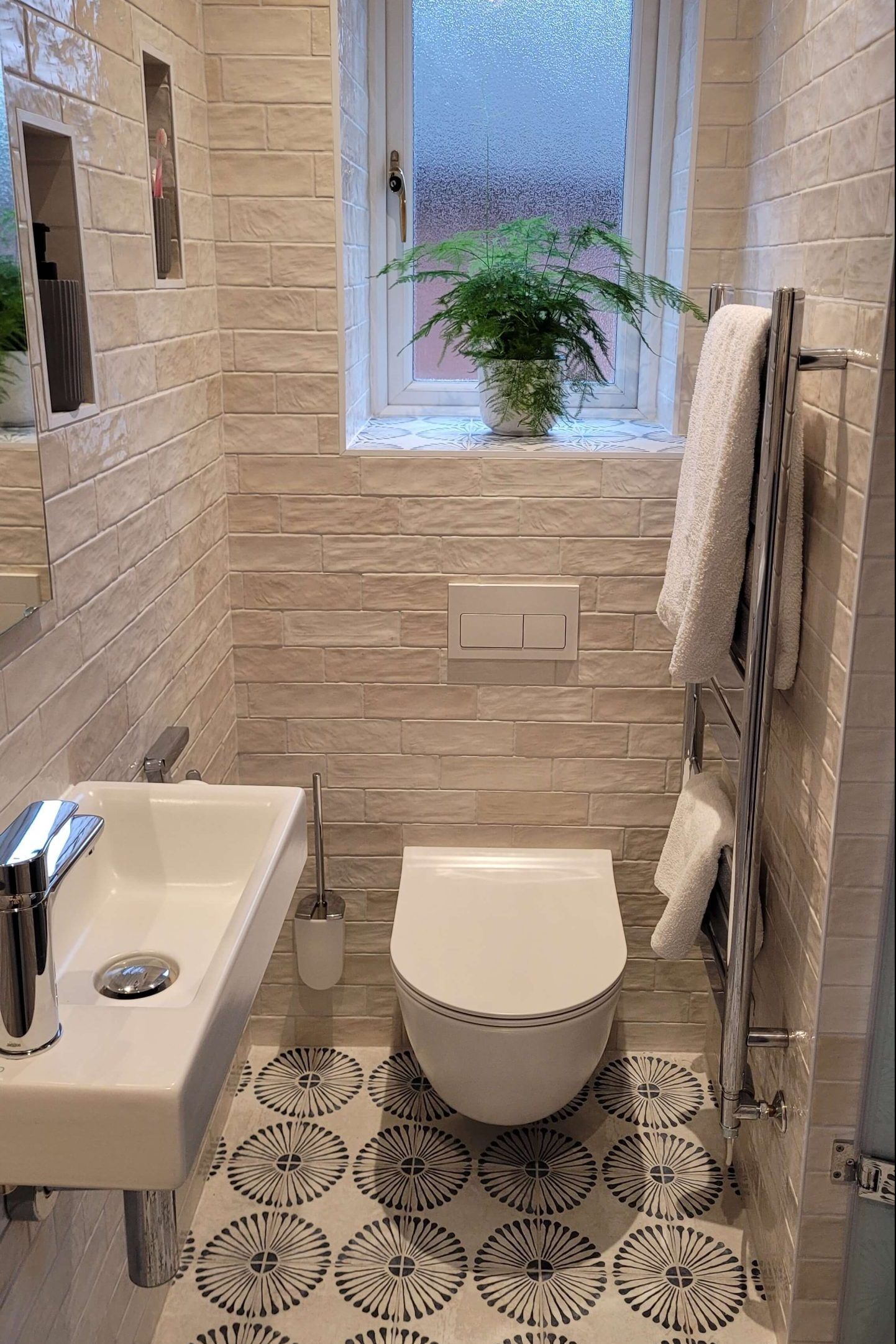 Narrow modern bathroom featuring a small floating sink, white subway tiles, and a large window with a potted plant