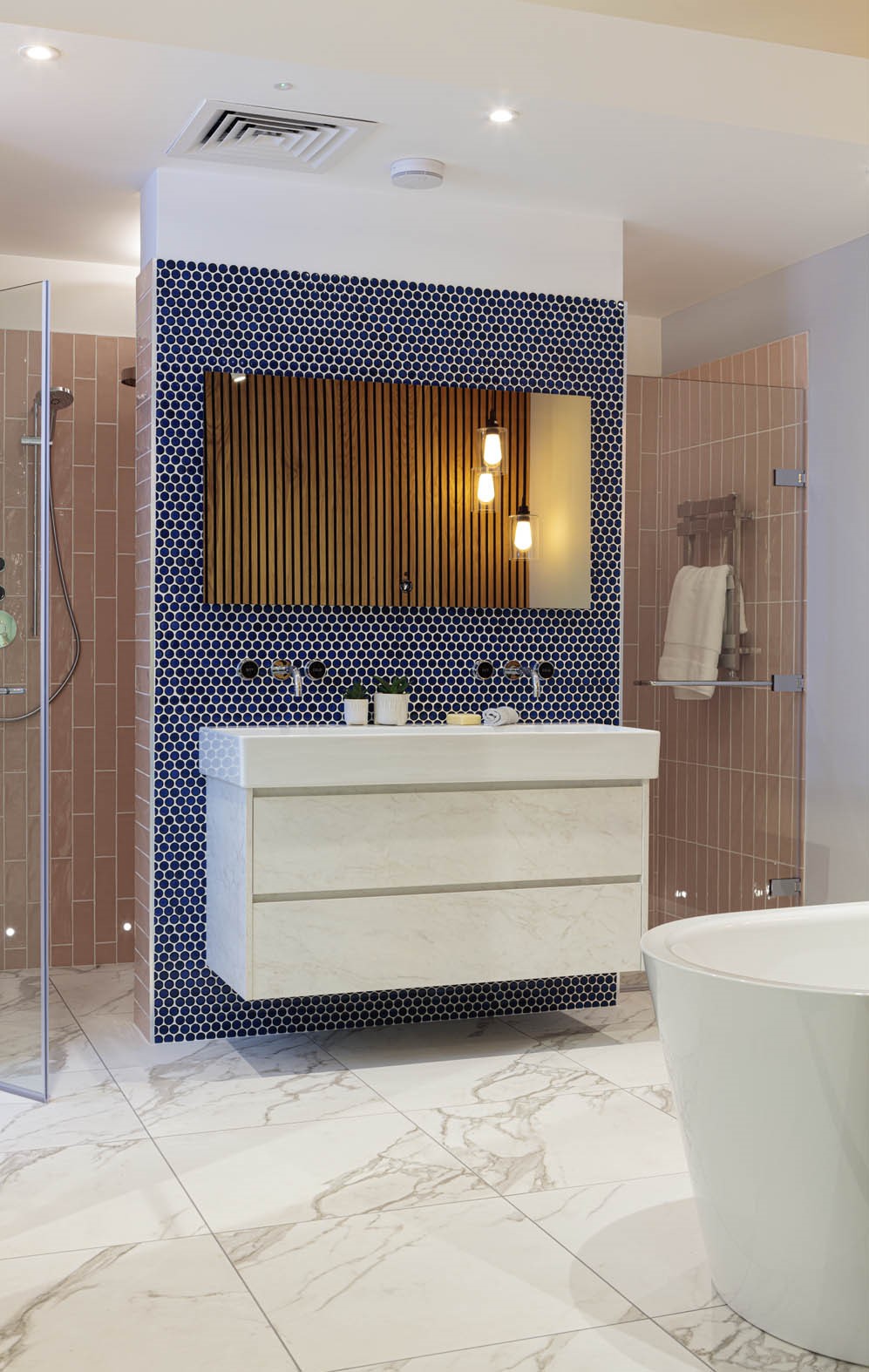 Modern bathroom with a floating vanity unit, marble effect floor tiles, blue hexagonal mosaic wall tiles, wooden slat feature wall, and glass-enclosed shower with blush pink tiles