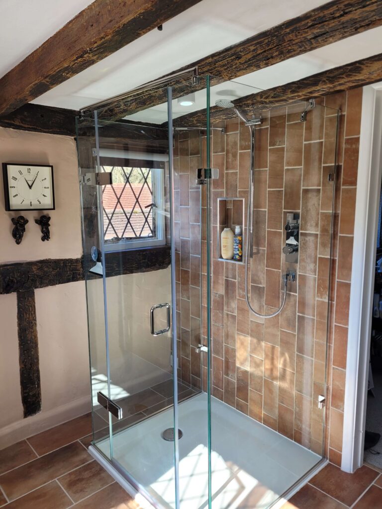 Modern glass-enclosed shower with exposed brick-style tiles, chrome shower fittings, and rustic wooden beams on the ceiling
