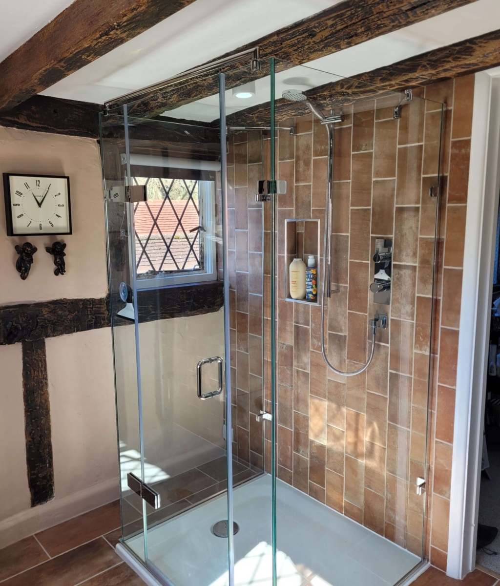 Modern glass-enclosed shower with exposed brick-style tiles, chrome shower fittings, and rustic wooden beams on the ceiling