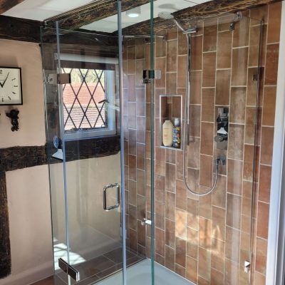 Modern glass-enclosed shower with exposed brick-style tiles, chrome shower fittings, and rustic wooden beams on the ceiling