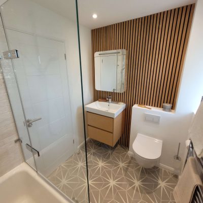 Scandinavian-style bathroom with wooden slatted wall, floating wooden vanity unit, geometric floor tiles, and a modern sink