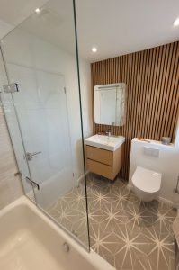 Scandinavian-style bathroom with wooden slatted wall, floating wooden vanity unit, geometric floor tiles, and a modern sink