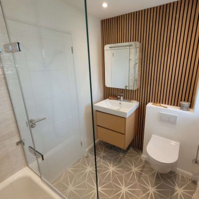 Scandinavian-style bathroom with wooden slatted wall, floating wooden vanity unit, geometric floor tiles, and a modern sink