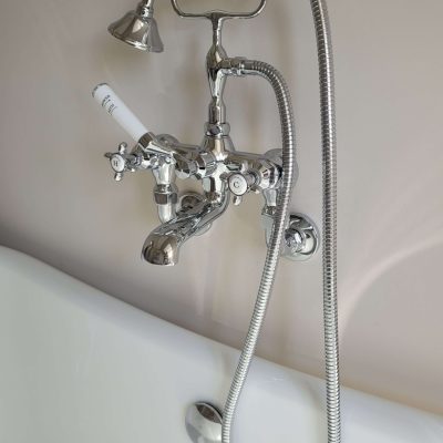 Close-up of a vintage chrome bathtub faucet with white porcelain handles, featuring a handheld shower attachment