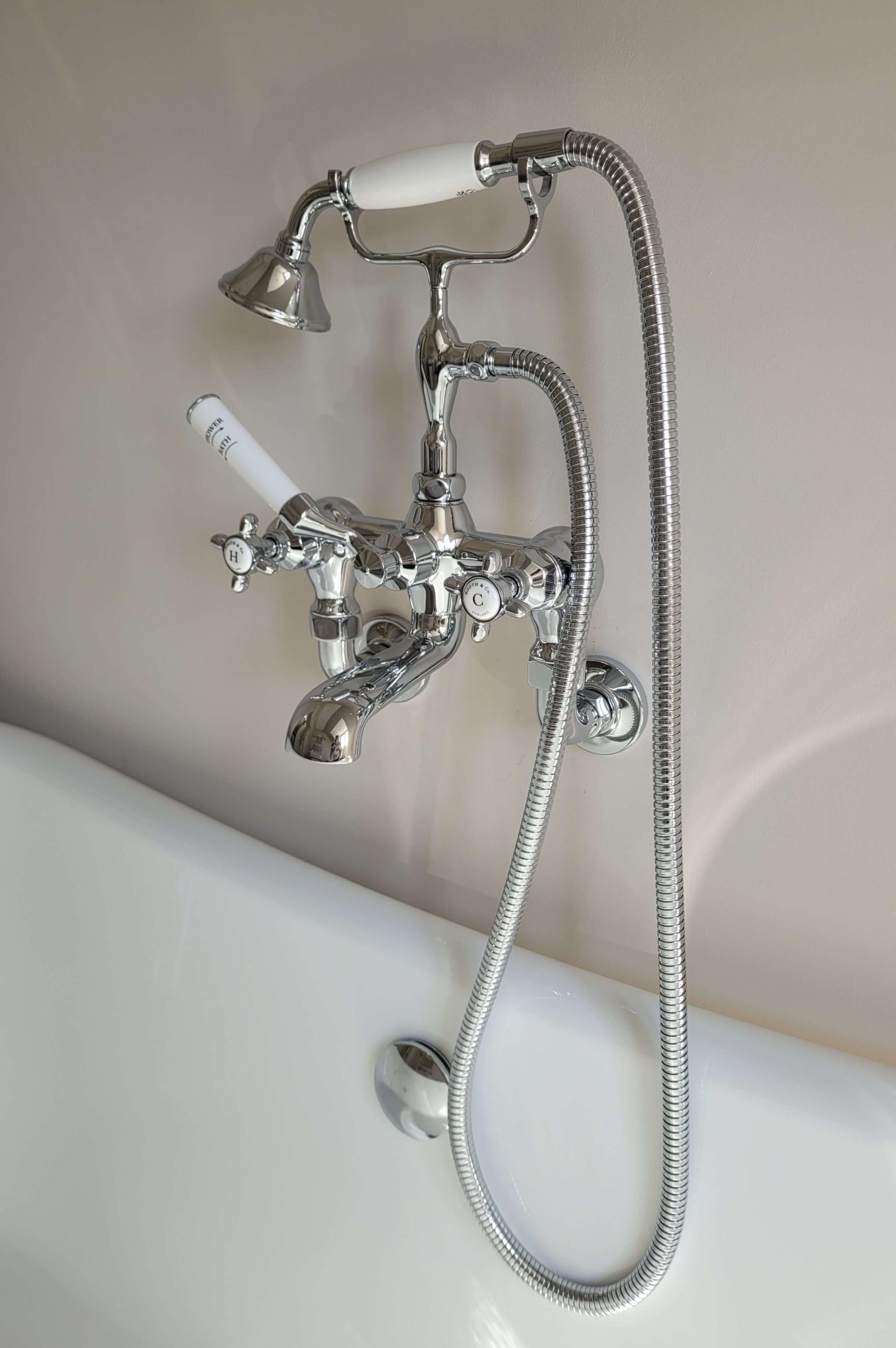 Close-up of a vintage chrome bathtub faucet with white porcelain handles, featuring a handheld shower attachment