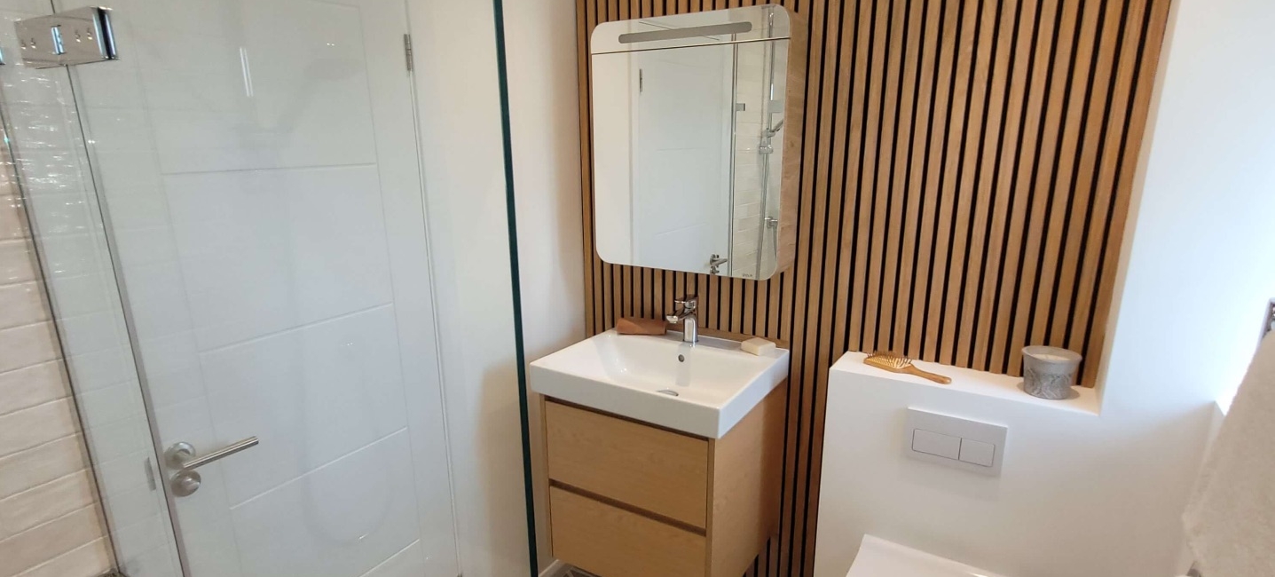 Modern bathroom features wood-panelled wall, geometric floor tiles, and a floating vanity unit.
