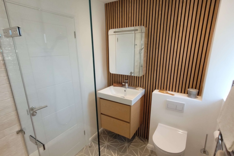 Modern bathroom features wood-panelled wall, geometric floor tiles, and a floating vanity unit.