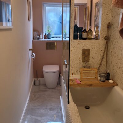 narrow bathroom with blush pink walls, terrazzo tiles in the shower, and gold fixtures