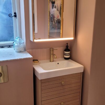 contemporary bathroom with blush pink walls, a wooden vanity with gold handles