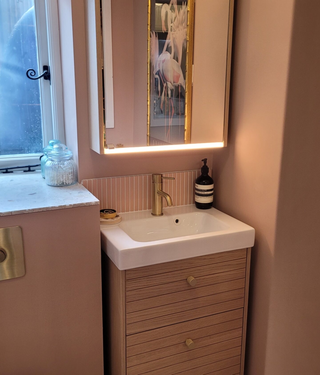 contemporary bathroom with blush pink walls, a wooden vanity with gold handles