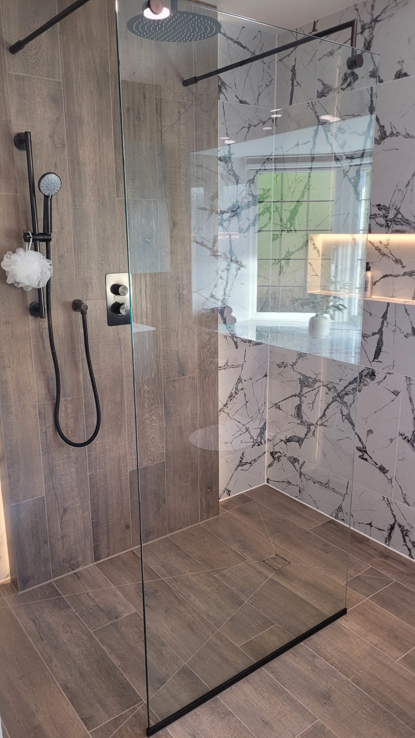 spacious walk-in shower with wood-effect tiles, marble feature walls, and a black rainfall showerhead